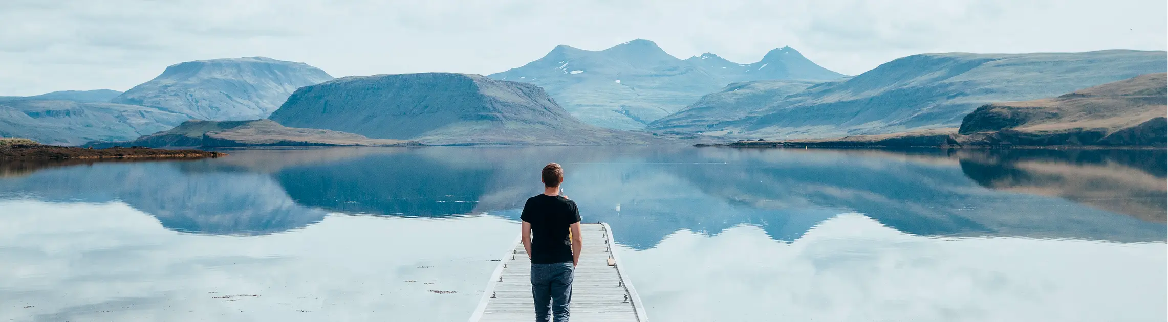 Photo of a single person standing on a pier, gazing over the water at mountains, considering their individual capacity for leadership in disruption